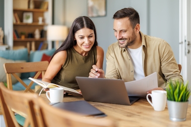 Couple at wood dining table reviewing finances on laptop.