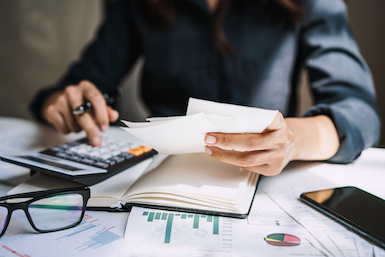 Woman with calculator and bank statement calculating contribution to investor checking account.