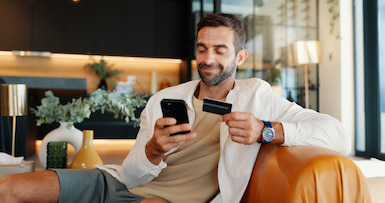 man holding mobile phone and debit card to access Stillman Online Banking Account