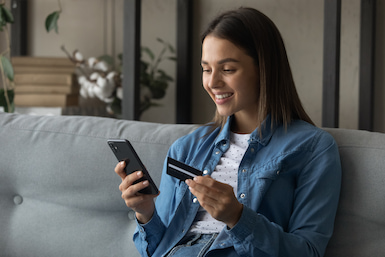 Young female student holding mobile phone and debit card checking Stillman student account balance